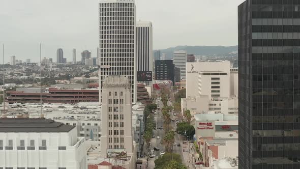 AERIAL: Flight Over Wilshire Boulevard Close To Street and Buildings with Car Traffic in Los Angeles