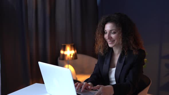 Attractive Curlyhaired Business Woman is Typing Text on a Laptop Keyboard and Smiling