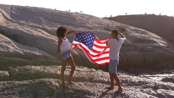 Couple holding American flag on rock at beach in the sunshine 4k