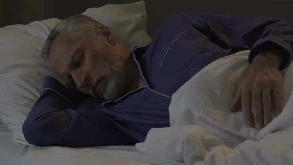 Senior Man Lying in Bed and Sleeping in Dark Room, Restoring Energy at Night