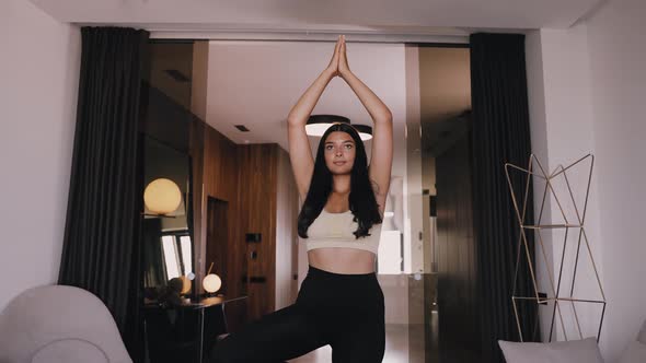 A Young Darkskinned Brunette Stands on One Leg Stretches Her Folded Arms Up