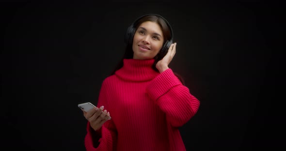 Woman in a Bright Pink Sweater Listens to Music with Headphones Through Phone