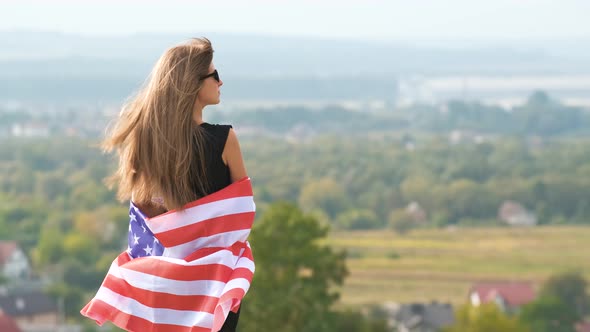 Young happy woman with long hair holding waving on wind american national flag on her 