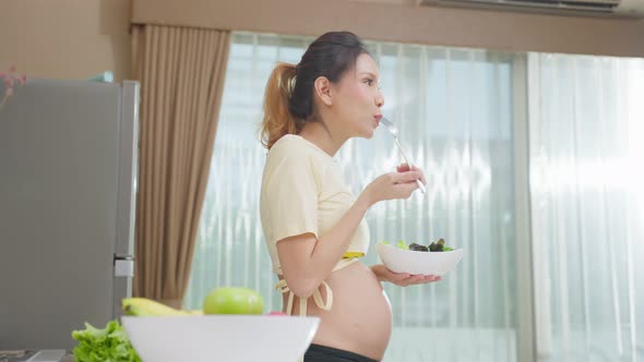 Asian beautiful pregnant woman eating healthy food in kitchen at home.