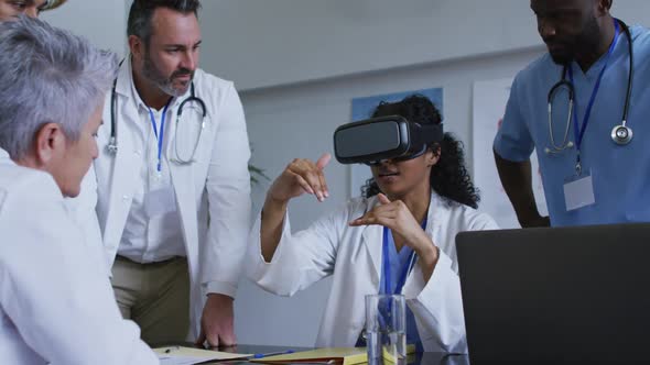 Asian female doctor at table using vr headset with a diverse group of colleagues gathered around her