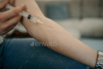 Selective focus shot of a person injecting medicine from a syringe at home