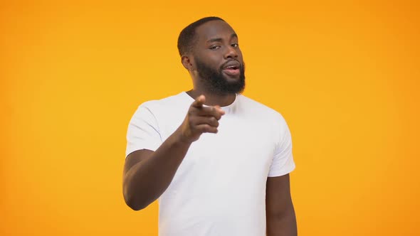 Smiling Black Man Pointing Finger, Winking Knowingly Against Yellow Background