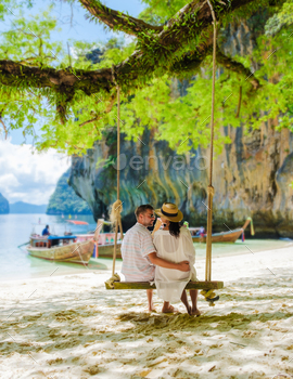 beautiful beach with longtail boats, a couple of European men, and an Asian woman on the beach relaxing on a swing under a tree. Couple on a boat trip