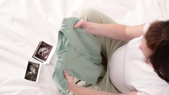 Top View Pregnant Mother Holding Baby Clothes in Hands Happy Expectant Mother Waiting Child