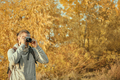 Man with a backpack looks into the camera viewfinder. Autumn time, trees with yellowed foliage.  - PhotoDune Item for Sale