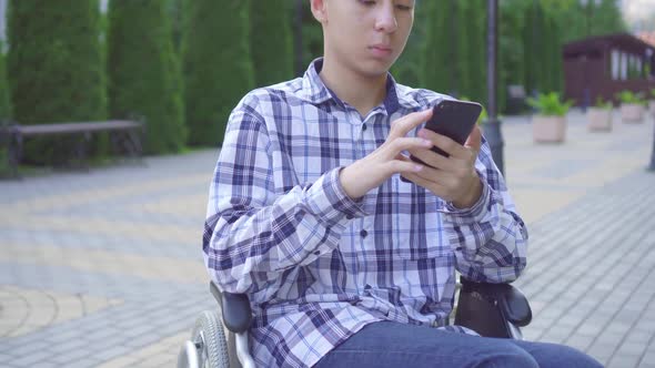 Young Asian Man Disabled in a Wheelchair in the Park and Uses a Smartphone