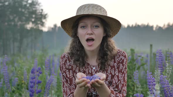 Woman in Straw Hat Blows Off Purple Petals of Lupin Flowers