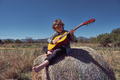 Boy playing acoustic guitar on hay roll in meadow - PhotoDune Item for Sale