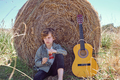 Upset kid sitting near guitar and leaning on hay bale - PhotoDune Item for Sale