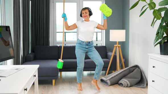 Woman in Headphones Cleaning the House and Having Fun Dancing with a Broom and Washcloth