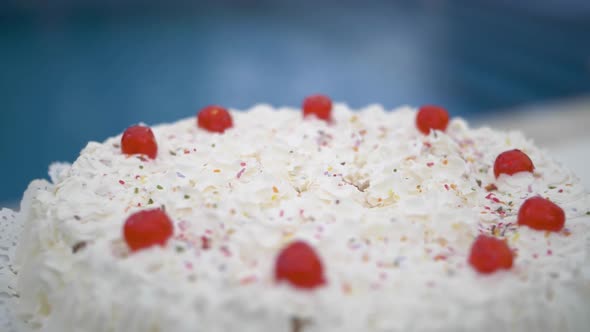 Sweet homemade white birthday cream cake with red candy cherries and colorful sprinkles at garden ev