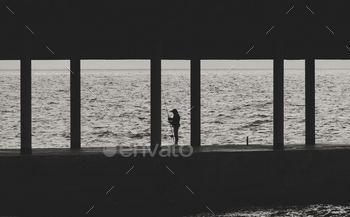 Silhouette of fisherman with fishing rod on pier