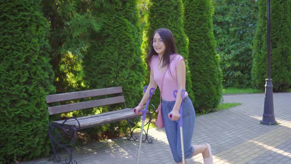 Young Positive Asian Woman with Broken Leg on Crutches Walking in the Park