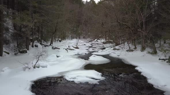 Drone flying backwards above snowy river rapids