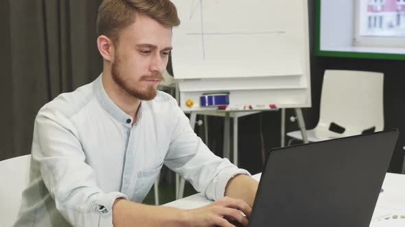 Attractive Young Man Using His Smart Phone and Laptop at the Office