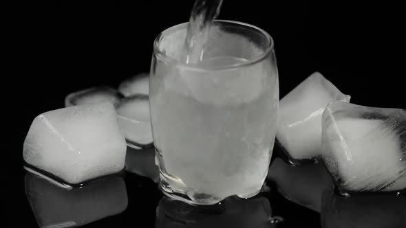 Pour Vodka Into Icy Glass with Ice Cubes Placed on a Black Background
