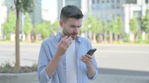 Young Man Reacting to Loss on Smartphone Outdoor