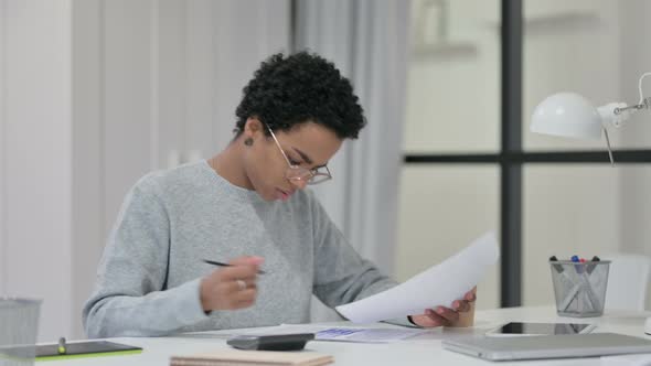 African Woman Using Calculator While Writing on Paper 