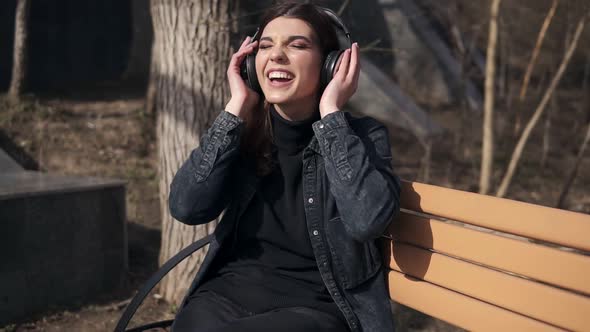 Beautiful Attractive Young Girl in Black Jeans Jacket is Sitting on the Bench in Park Enjoying