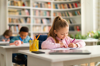 Group of smart school children sitting at desks in classroom or library at primary school, writing