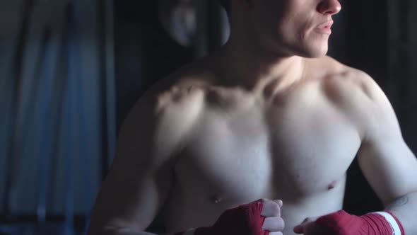 Cinematic shot tilting up across the sexy muscular body of a young MMA fighter who turns to look dir