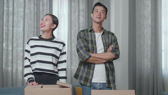 Smiling Young Asian Couple Carrying Cardboard Boxes With Stuff Into A New House Then Looking Around