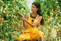 Sitting and working. Young woman in yellow uniform is in garden with vegetables - PhotoDune Item for Sale
