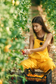 Sitting and working. Young woman in yellow uniform is in garden with vegetables - PhotoDune Item for Sale