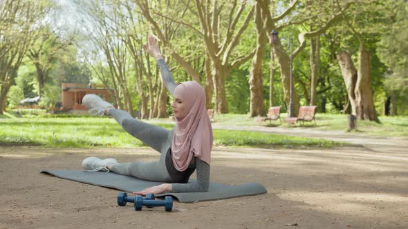 Smiling Young Woman in Hijab and Sport Outfit Doing Flexible Exercises on Yoga