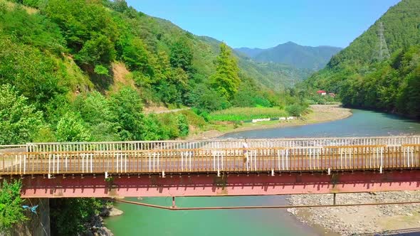 Aerial side view of a man crossing a bridge in Georgia over the Chorokhi River,