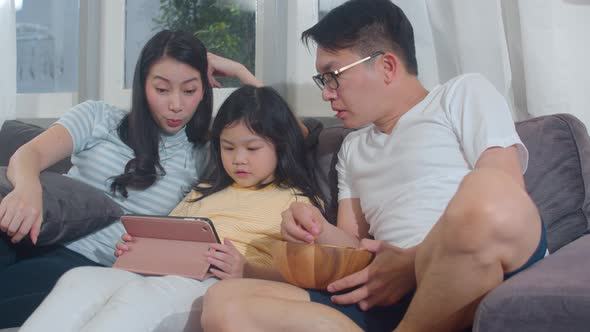 mother, father relax with little girl watching movie lying on sofa in living room.