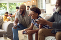 Multi-Generation Male Family Sitting On Sofa At Home Playing Video Game With Dad Cheating - PhotoDune Item for Sale