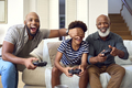 Multi-Generation Male Family Sitting On Sofa At Home Playing Video Game With Dad Cheating - PhotoDune Item for Sale
