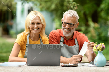 ors in their garden, smiling mature spouses accounting on computer, planning family finances and checking bills, enjoying successful economy