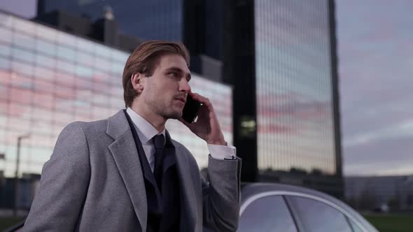Portrait of a Elegant Businessman Standing Near a Business Car and Talking on a Mobile Phone Top