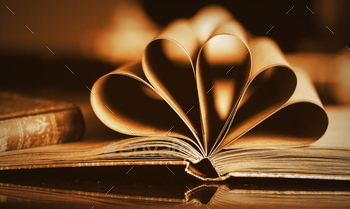 Close up view of old book with heart shaped pages on wooden table.