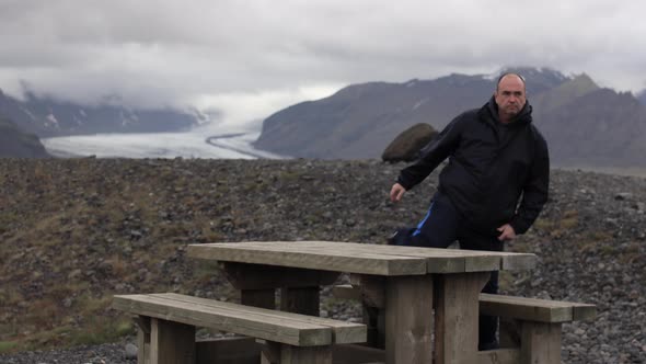 Man sitting at Picnic table with a mountain in the background