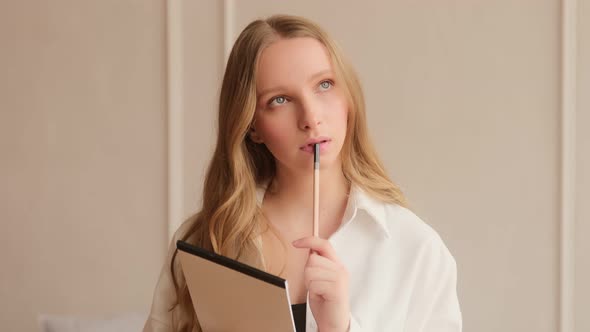 Young inspired woman pensively thinks and making notes in paper notebook