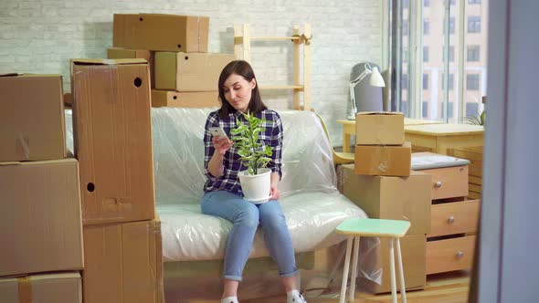 Joyful Woman Uses the Phone Sitting on the Couch After Moving in Modern Apartment