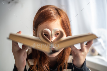 A girl is holding a book. Heart-shaped pages. Reading, Knowing, Learning