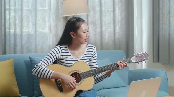 Asian Woman With Laptop Singing And Playing Guitar At Home