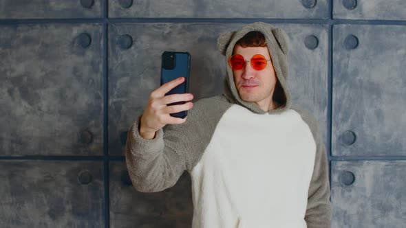 Young Man in Hood with Ears and Orange Glasses with Mobile Phone Near Patterned Concrete Wall