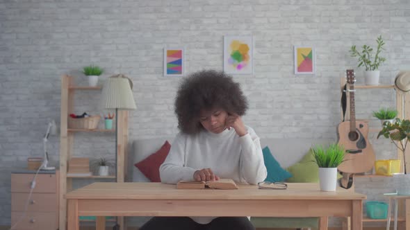 African American Woman with an Afro Hairstyle Reading a Book at the Table