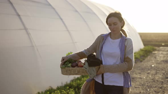 Blonde Woman Walking Near the Greenhouse Carrying Fresh Vegetables or Plants