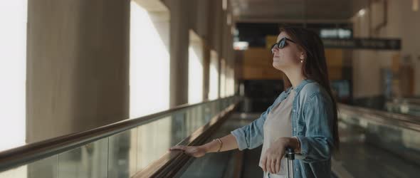 Woman with Suitcase Standing on a Moving Walkway of an Airport